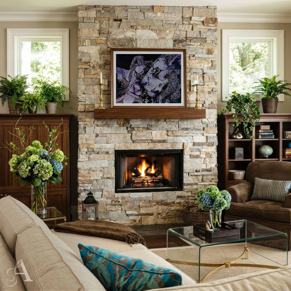 A styled living room featuring a large stone fireplace with a wood mantel and framed artwork, a lit fire in the fireplace opening, a beige sofa with blue patterned pillows, a glass coffee table, and potted plants.