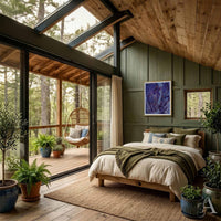 A rustic, cozy bedroom with a wooden bed, beige bedding, and a green paneled wall, featuring large glass windows that open onto a wooden deck with a hanging chair and forest view. Purple framed artwork of horses and a dog on the wall.