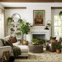 A beautifully styled living room featuring a white shiplap wall, a fireplace with a framed painting above it, a striped chaise lounge, a wicker armchair, and multiple potted green plants.