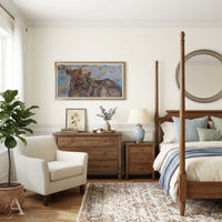 A styled bedroom interior featuring a wooden four-post bed, matching wooden nightstand and dresser, a cream armchair, a potted plant, and a large framed painting of a deer on the wall.